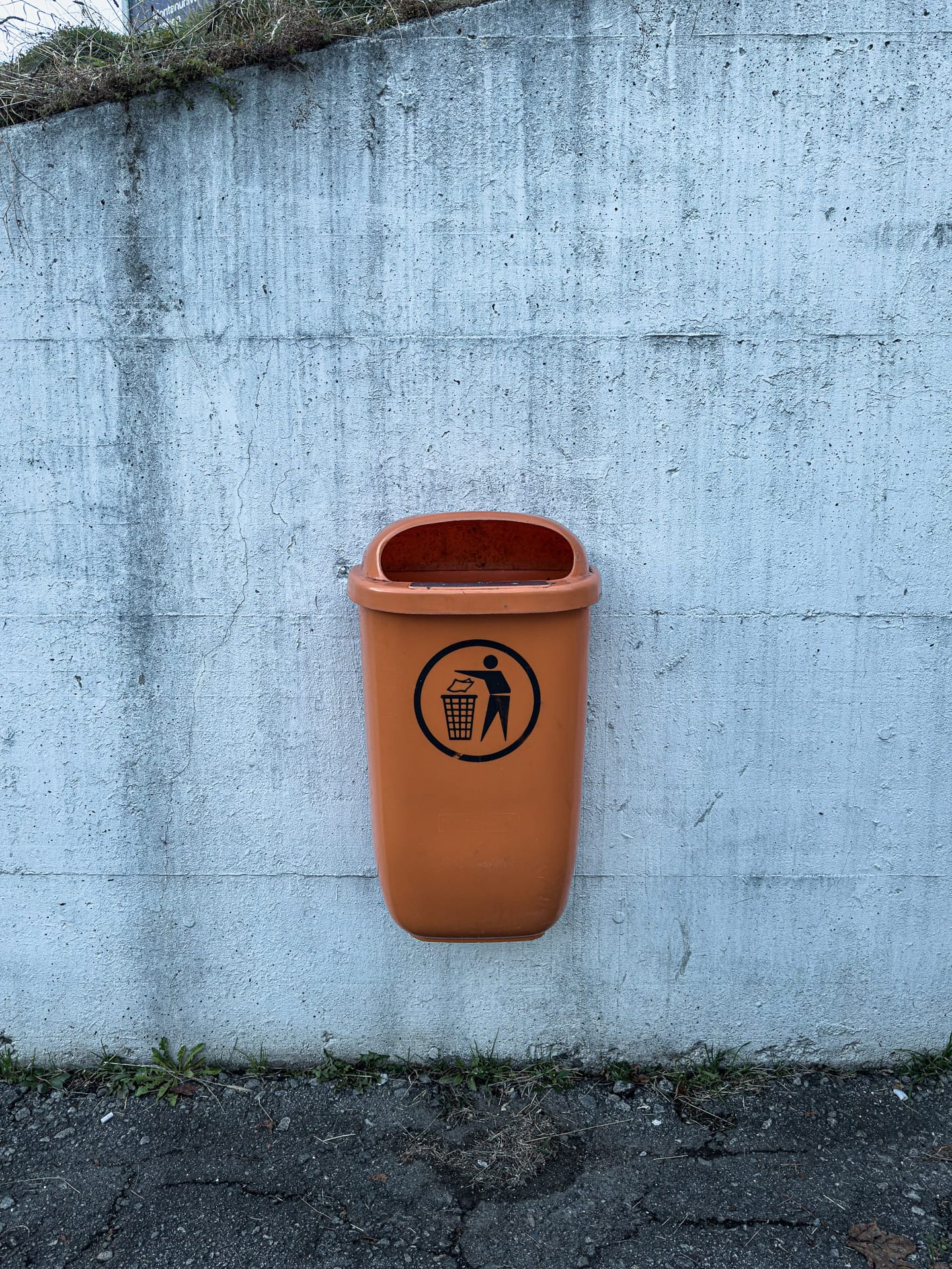 Public trash bin mounted on a concrete wall in Zeltweg, Austria.